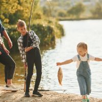 Weekend activities. Father and mother with son and daughter on fishing together outdoors at summertime.